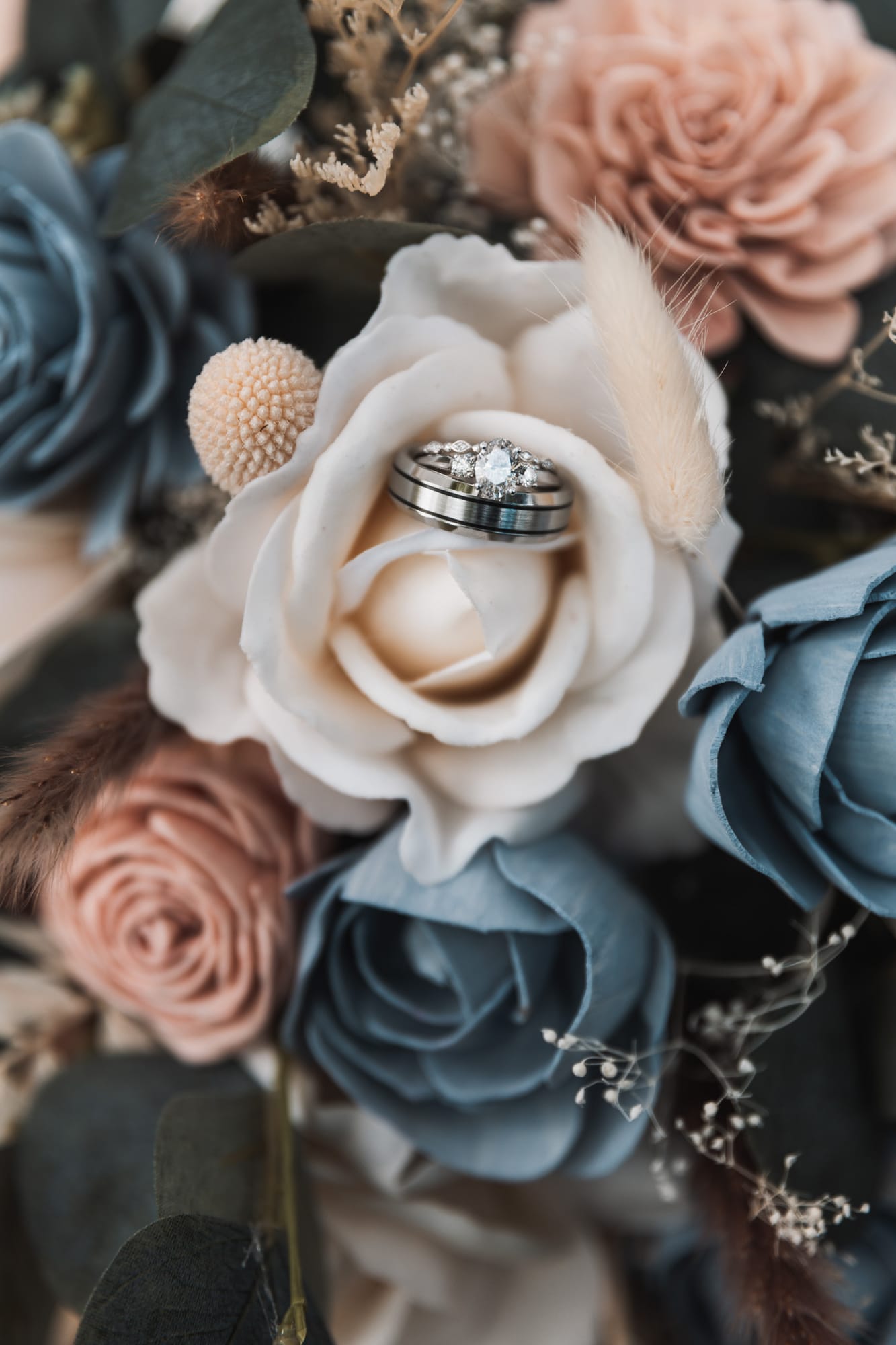 Wedding rings nestled in a dusty blue and blush bridal bouquet