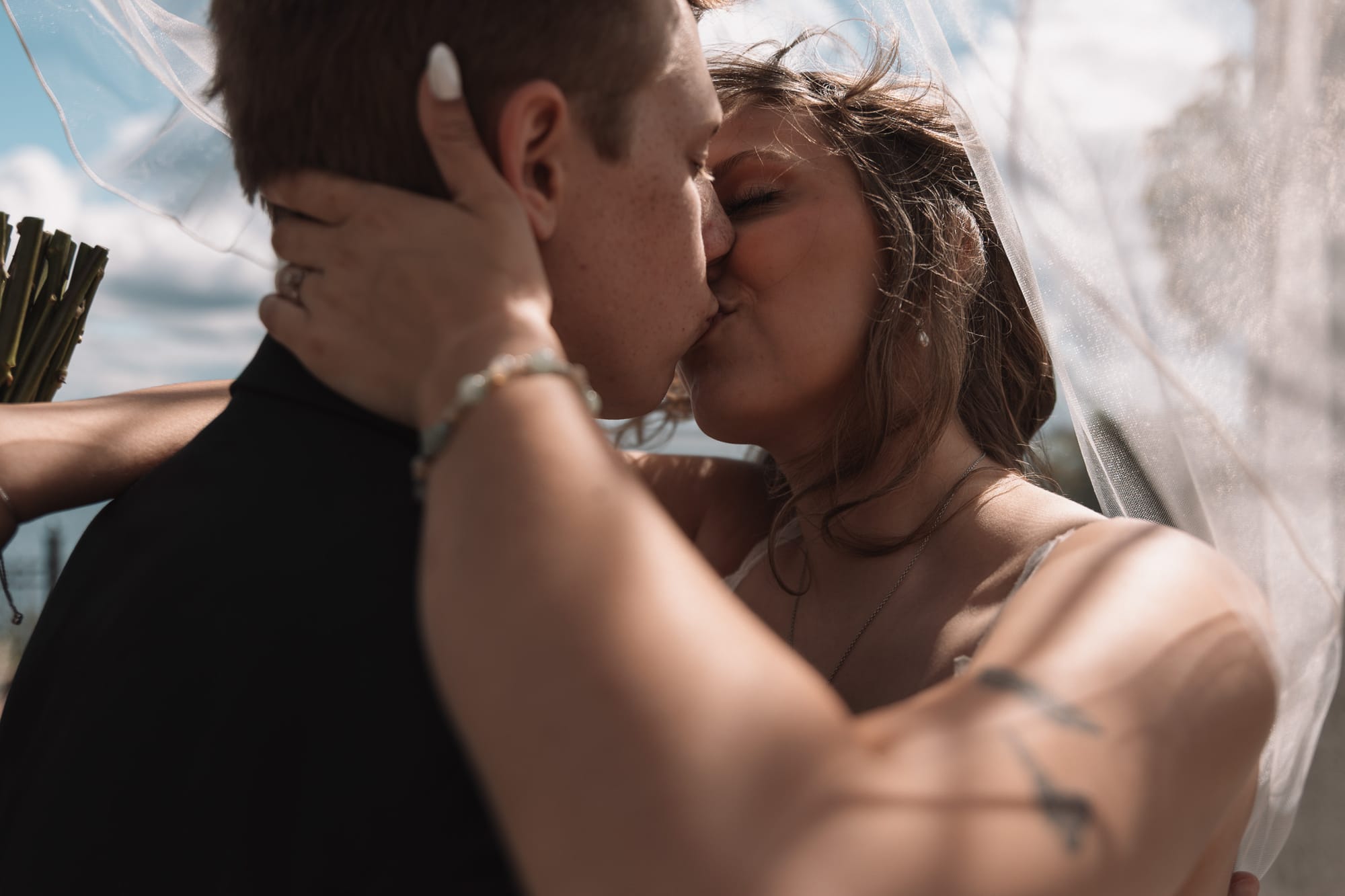 Bride and groom kissing beneath a veil on their wedding day