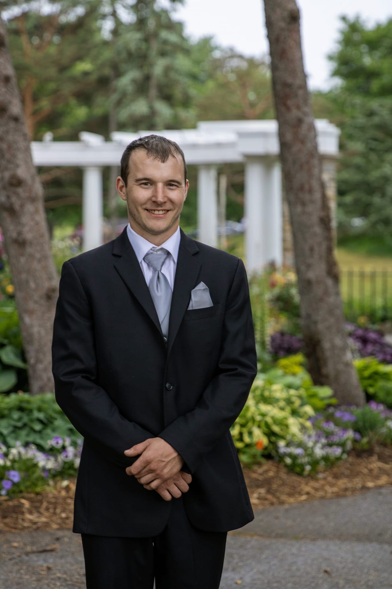Groom portrait in a black suit among garden flowers